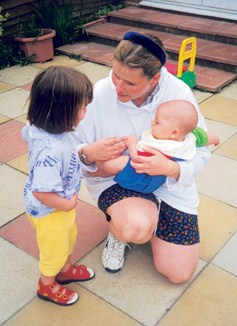 A picture of a lady hold a baby with a little girl holding the babies hand